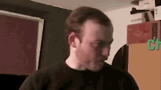 a man in a black sweater is standing in a room with a green sign that says ch .