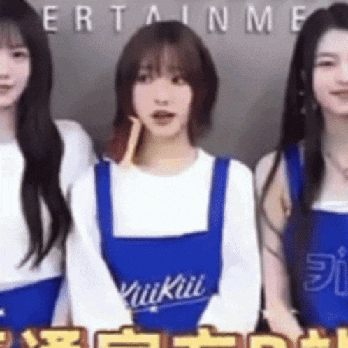 three women are standing next to each other wearing blue aprons that say ' kuikiii ' on them .