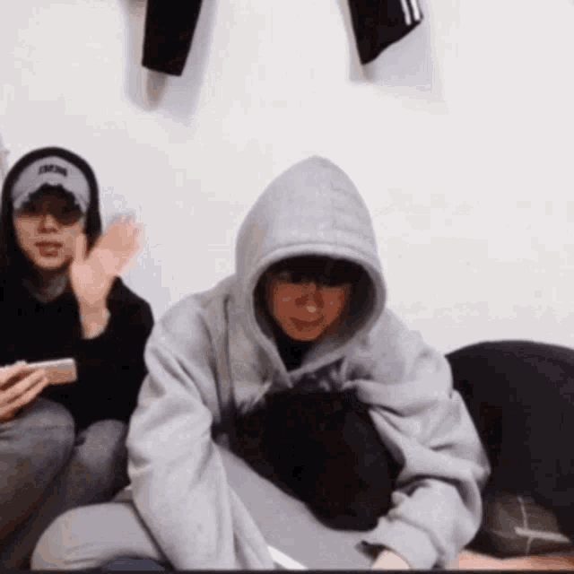 a man wearing a hat that says ' jackson ' on it sits next to another man wearing a hoodie