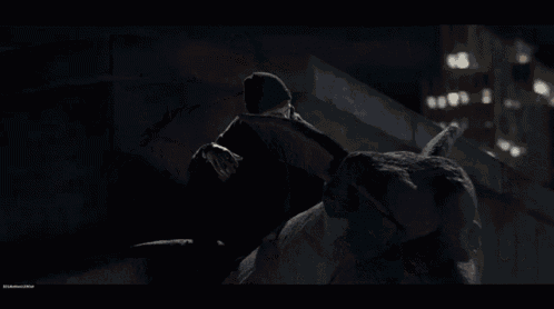 a man in a black hat is standing on a rooftop at night looking at his watch