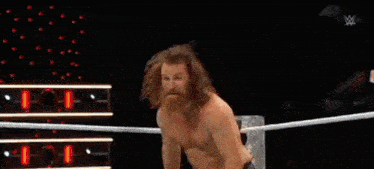 a man with a beard and long hair is standing in a ring without a shirt on .