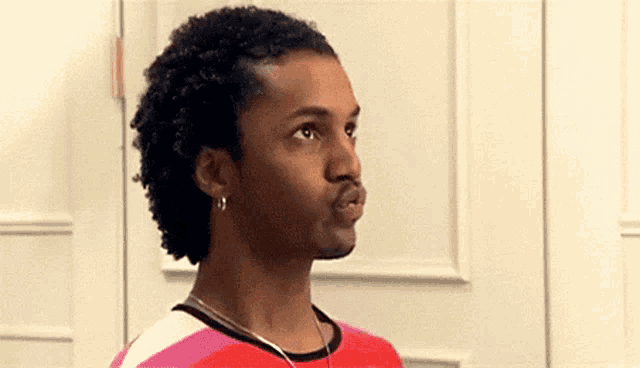 a man with curly hair is wearing a red and pink striped shirt and earrings .