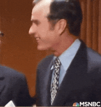 a man in a suit and tie shakes hands with another man in a tie