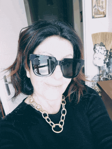 a woman wearing sunglasses and a gold chain around her neck smiles