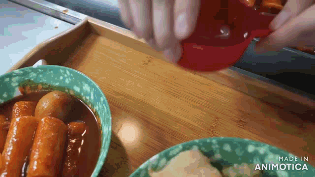 a person is pouring liquid from a red cup into a bowl of food on a wooden tray .