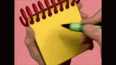 a person is writing on a yellow notepad with a green pen .