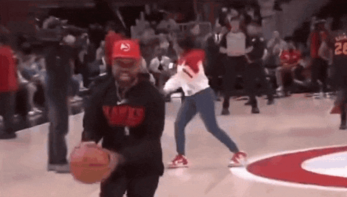 a man is holding a basketball on a basketball court while a woman tries to stop him .
