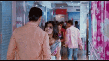 a man and a woman are walking down a hallway holding hands .