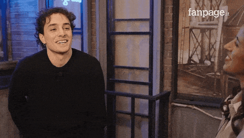a man in a black sweater is smiling in front of a fanpage advertisement