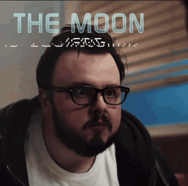 a man with glasses and a beard looks at the camera with the words the moon behind him