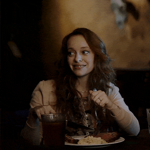 a woman is sitting at a table with a plate of food and a glass of beer
