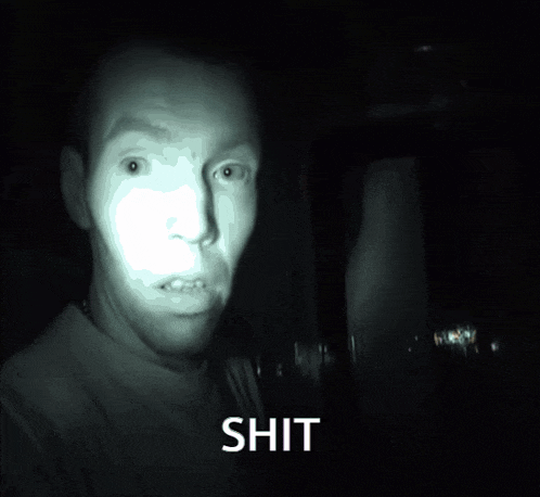 a man 's face is lit up in the dark and the word shit is on the bottom