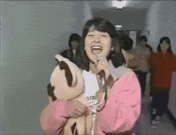 a woman in a pink jacket singing into a microphone while holding a stuffed animal