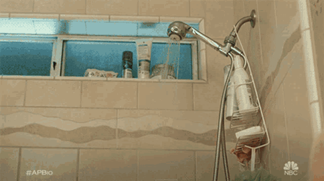 a shirtless man is taking a shower in a bathroom with a nbc logo on the wall