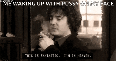 a man is smoking a cigarette and drinking a glass of wine while waking up with pussy on his face .