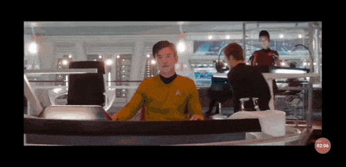 a man in a star trek uniform sits at a desk with a clock that says 02:04