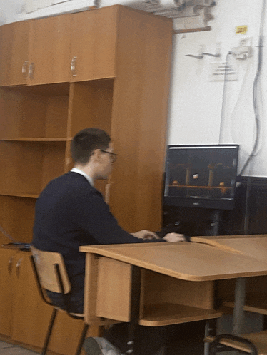 a man sits at a desk in front of a monitor that has a yellow sticker on it