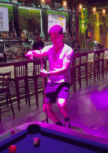 a man is kneeling on a pool table with a pool cue in his hand