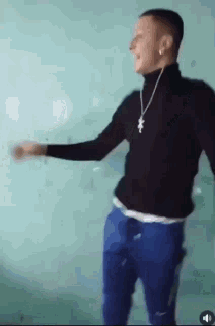 a man wearing a black turtleneck and blue shorts is dancing in front of a green wall .