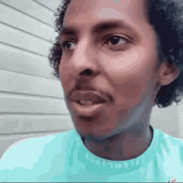 a man with curly hair and a beard is wearing a blue shirt and making a funny face .