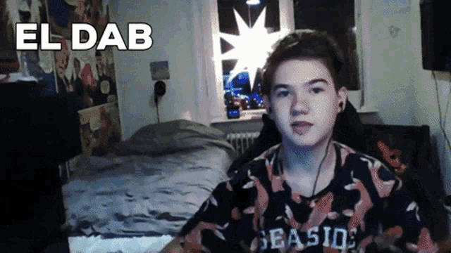 a boy wearing a seaside shirt is sitting in front of a bed