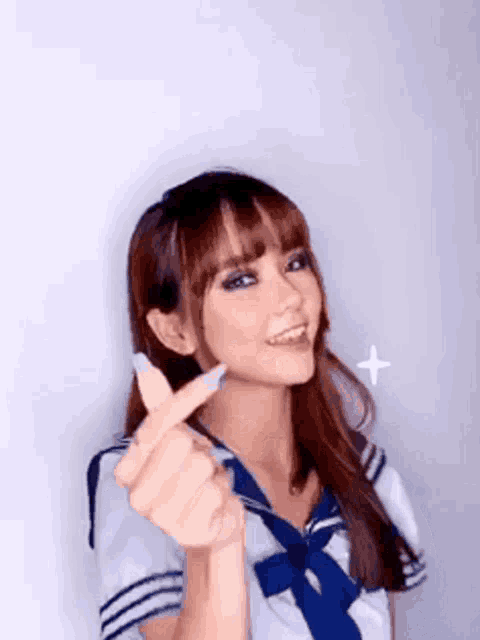 a young woman in a sailor suit is making a heart shape with her hands .