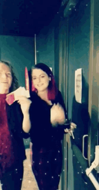 two women standing next to each other in front of a door with a sign on the wall that says no smoking