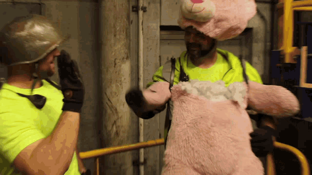 a man in a pink teddy bear costume talks to another man in a yellow shirt