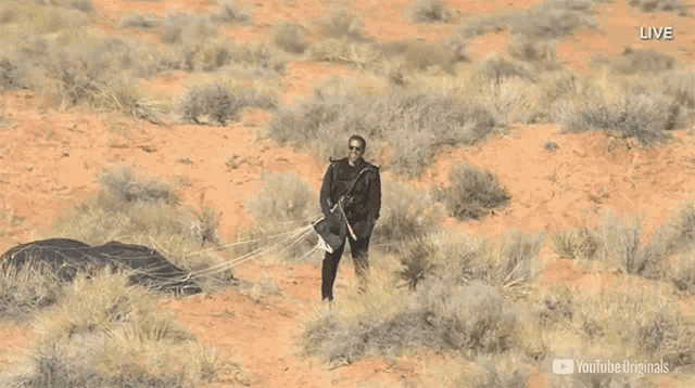a man in a black suit is standing in the desert with a youtube originals logo on the bottom right
