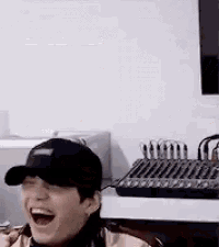 a man wearing a baseball cap is laughing in a room with a mixer in the background .
