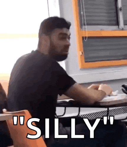 a man with a beard is sitting at a desk with the words " silly " written on it