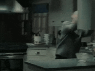 a man is standing in a kitchen with his arms outstretched and a sign that says `` docit bje '' .