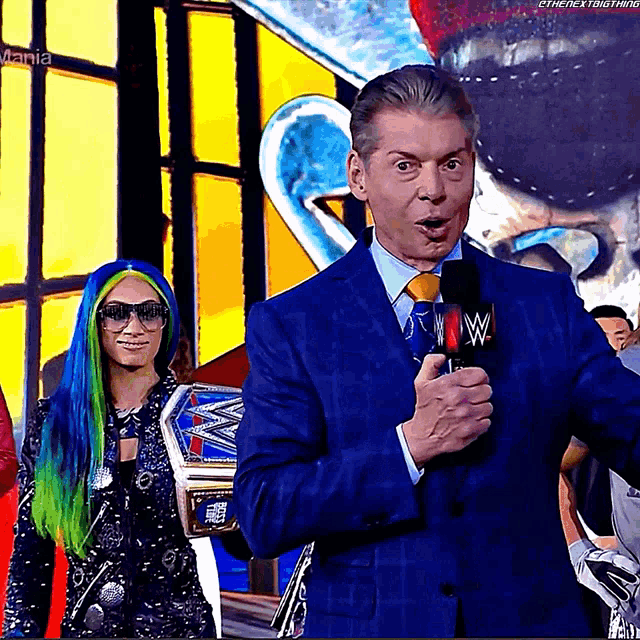 a man in a blue suit and tie is holding a microphone with the letters wwe on it