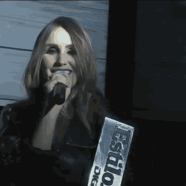 a woman is singing into a microphone while wearing a sign that says estilo dig