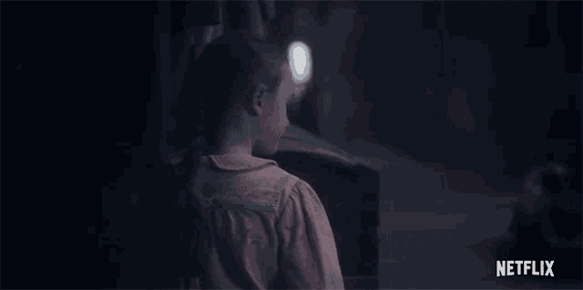 a girl in a pink shirt is standing in a dark room looking at something .