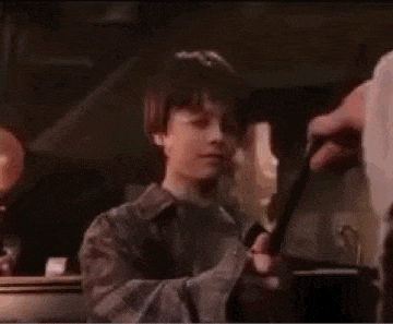 harry potter is holding a wand in his hand and looking at someone .