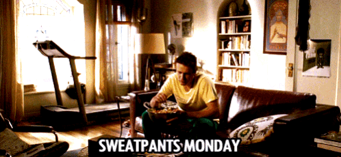 a man is sitting on a couch with a sign that says sweatpants monday on it