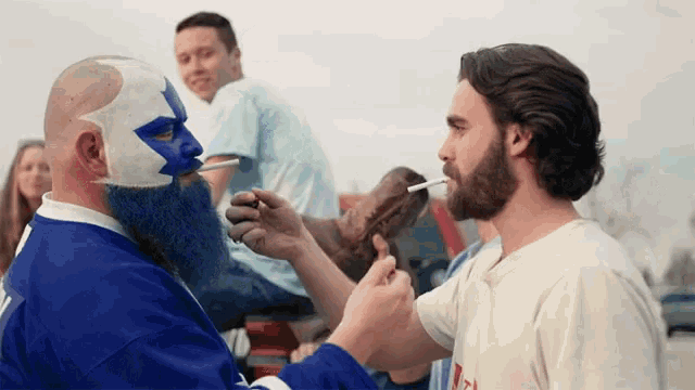 a man with a blue face paint and a beard is smoking a cigarette