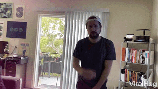 a man in a black shirt is dancing in a living room with a bookshelf that says viralhog