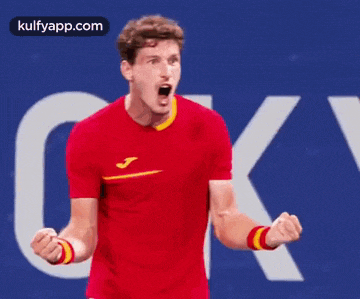 a man in a red shirt is holding his fist up in the air .