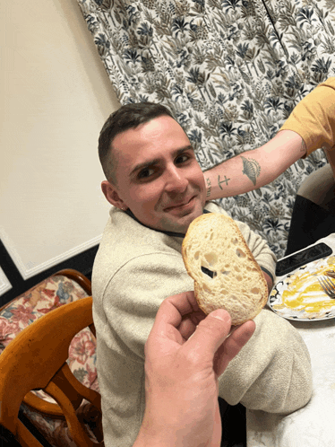 a man with a tattoo on his arm holds a piece of bread in front of his face