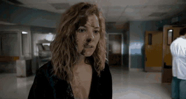 a woman with a lot of dirt on her face is walking down a hallway .