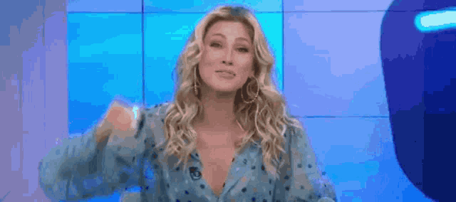 a blonde woman in a blue polka dot dress is standing in front of a blue wall and smiling .