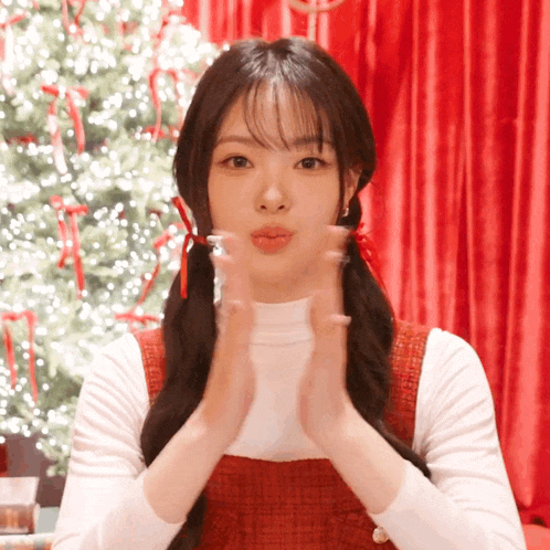a girl with pigtails blowing a kiss with a christmas tree in the background