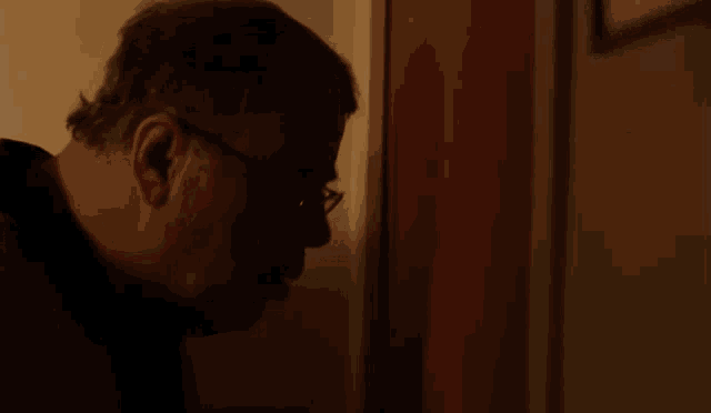 a man wearing glasses is looking through a door and the word ouvr is on the bottom