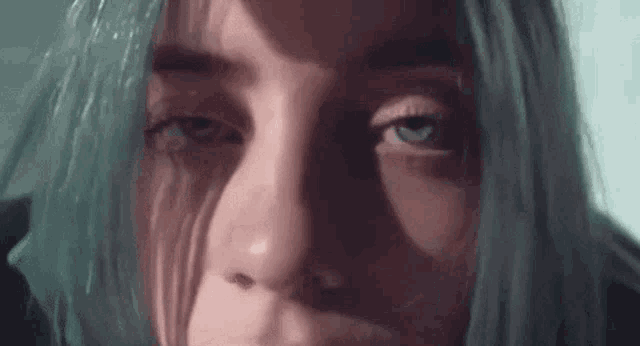 a close up of a woman 's face with green hair and tears running down her face .
