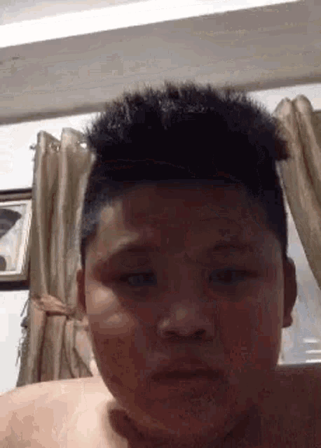 a young boy with a very short haircut is looking at the camera .