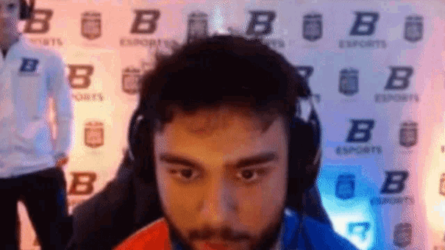 a man wearing headphones looks at the camera in front of a wall with letters b on it