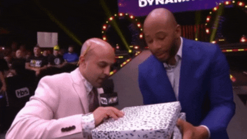 a man in a pink suit and a man in a blue suit are looking at a box with the word dynamite on it