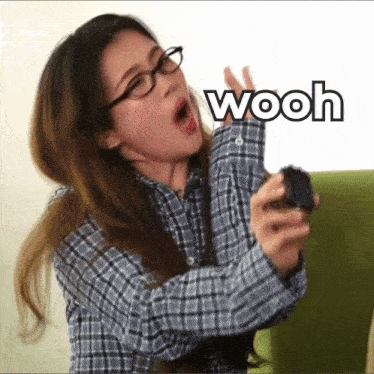 a woman wearing glasses and a plaid shirt is holding a remote control and says wooh